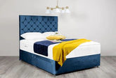 Blue upholstered bed with white mattress and yellow blanket in a room with a chandelier.