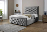 Gray tufted bed in a room with wooden flooring and a plant.
