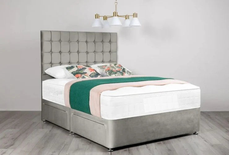 Gray upholstered bed with floral bedding and green blanket in a room with a chandelier.