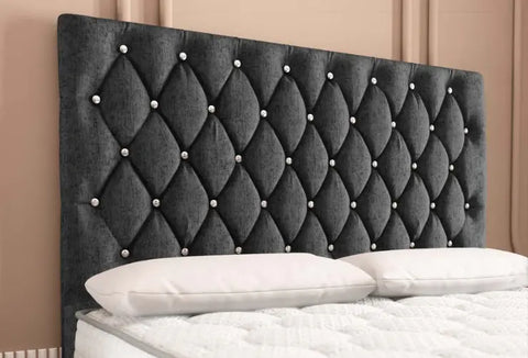 Gray tufted headboard with decorative nails on a bed against a beige wall.