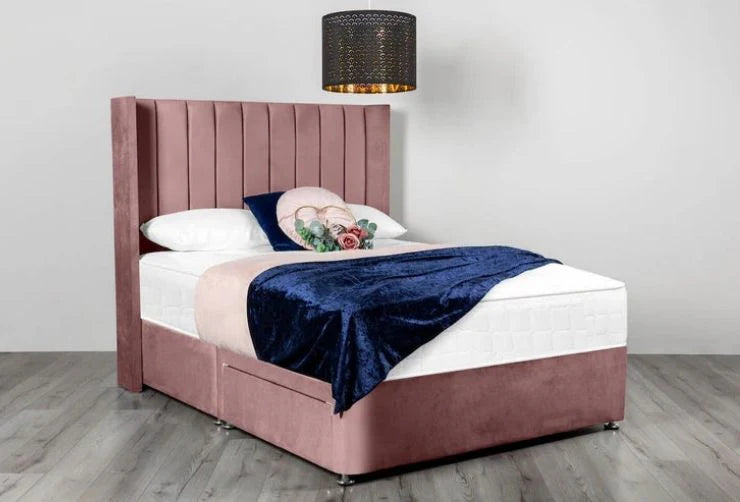 Pink upholstered bed with white bedding and a blue throw blanket in a room.