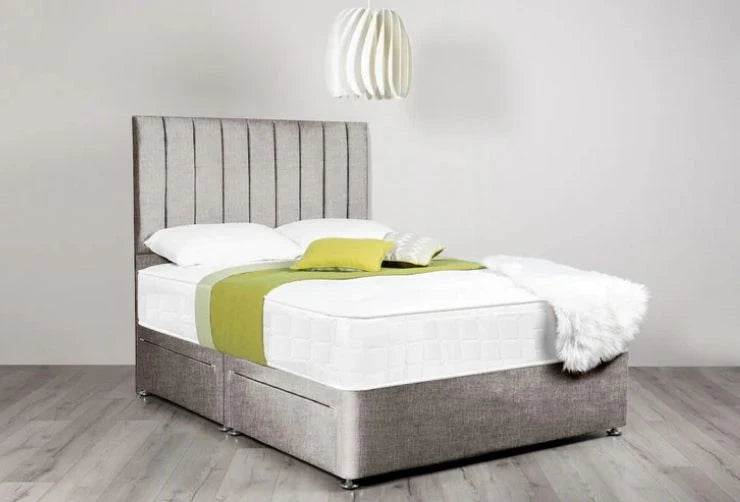 Bed with gray upholstered headboard and white bedding, green blanket, and white pillow on a wooden floor.