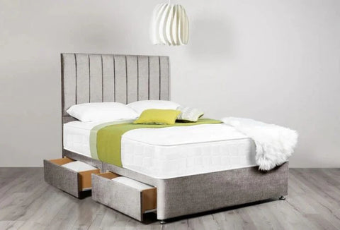 Gray upholstered bed with white bedding and green blanket in a room setting.