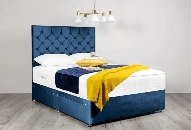 Blue upholstered bed with white mattress and yellow blanket in a room with a chandelier.